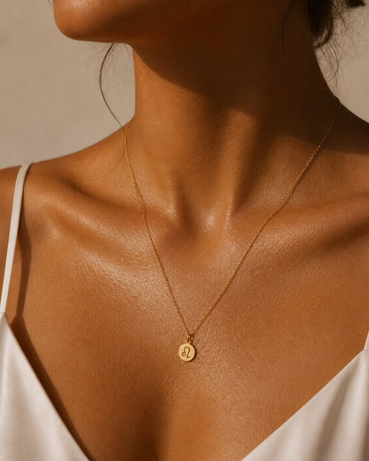 Kvinna som bär Rizo stjärntecken halsband med graverad berlock i guld